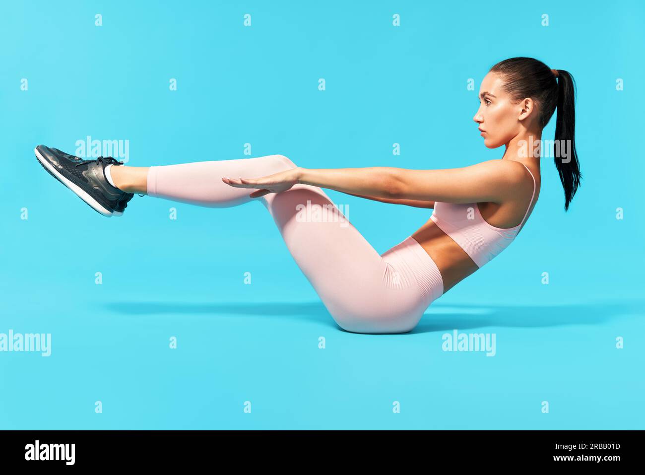Bella giovane donna in rosa sportswear facendo fitness esercizio sit-up, abs. Su sfondo blu Foto Stock