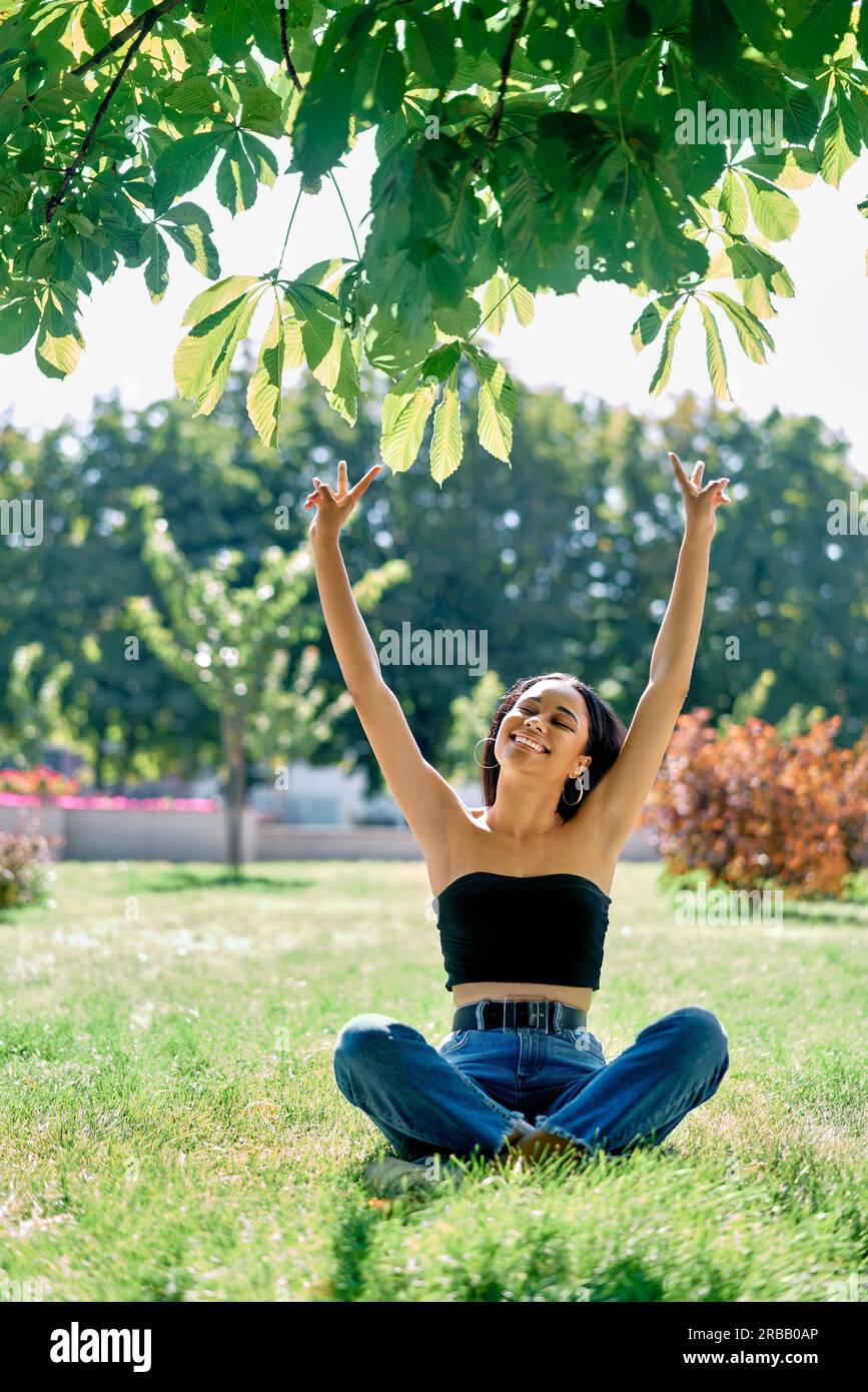 Libertà felice afro donna americana con le braccia in su rilassarsi nel parco. Successo, divertimento, vincere concetto Foto Stock