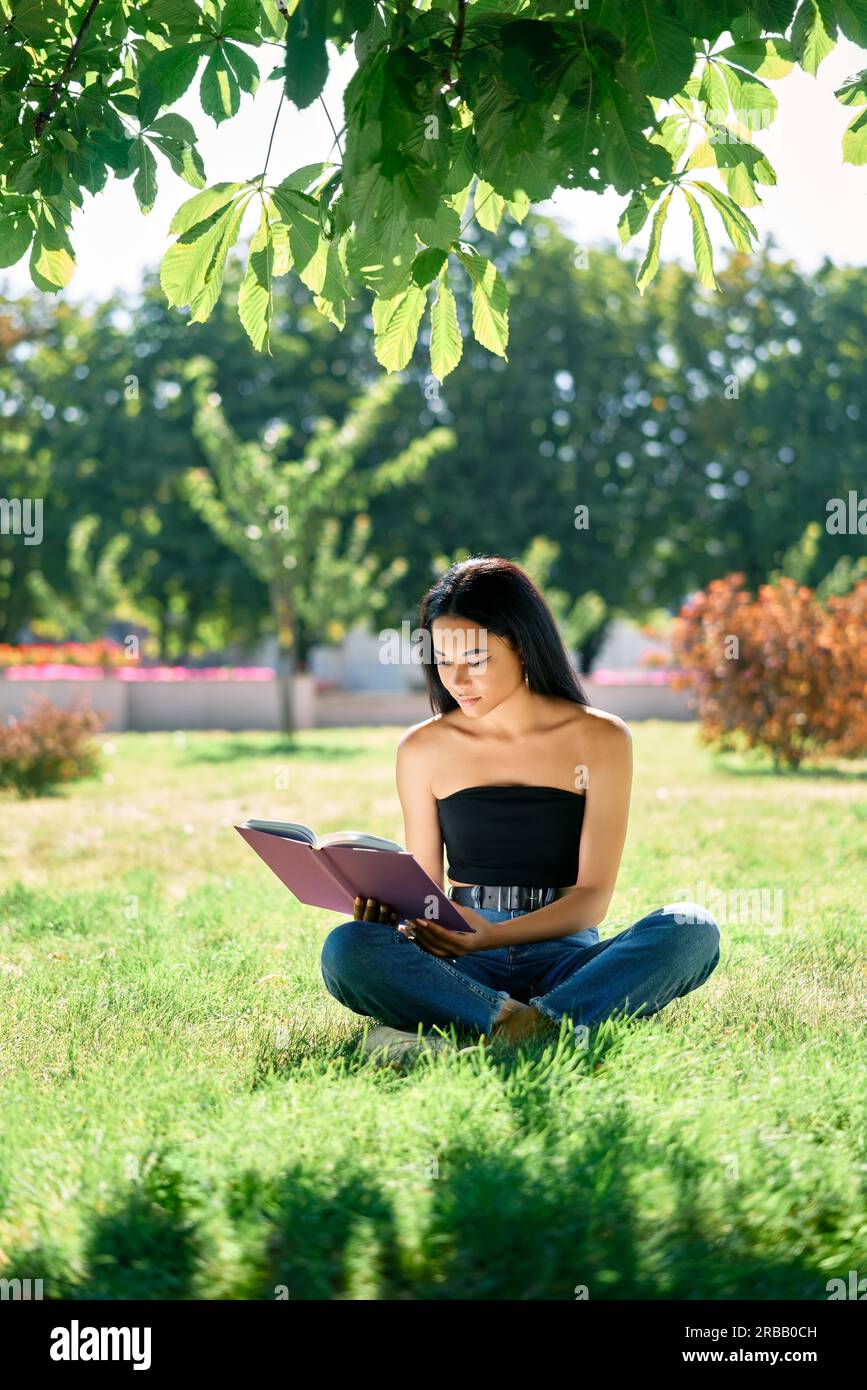 Piuttosto afro americano donna leggere libro sull'erba nel parco. Relax e hobby concetto Foto Stock