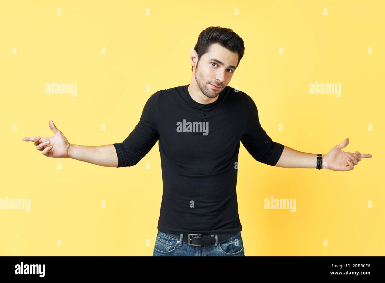 Un giovane confuso vestito di t-shirt nera ha un dubbio su sfondo giallo gesturing con le mani Foto Stock