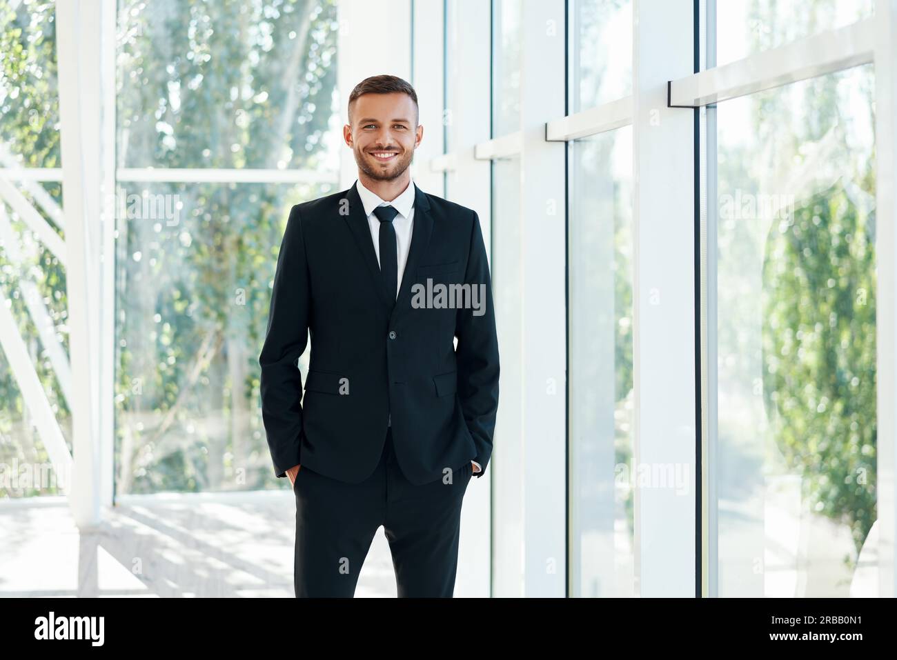 Uomo d'affari sorridente e sicuro in elegante suite in posa in un moderno ufficio creativo. Persone in affari Foto Stock