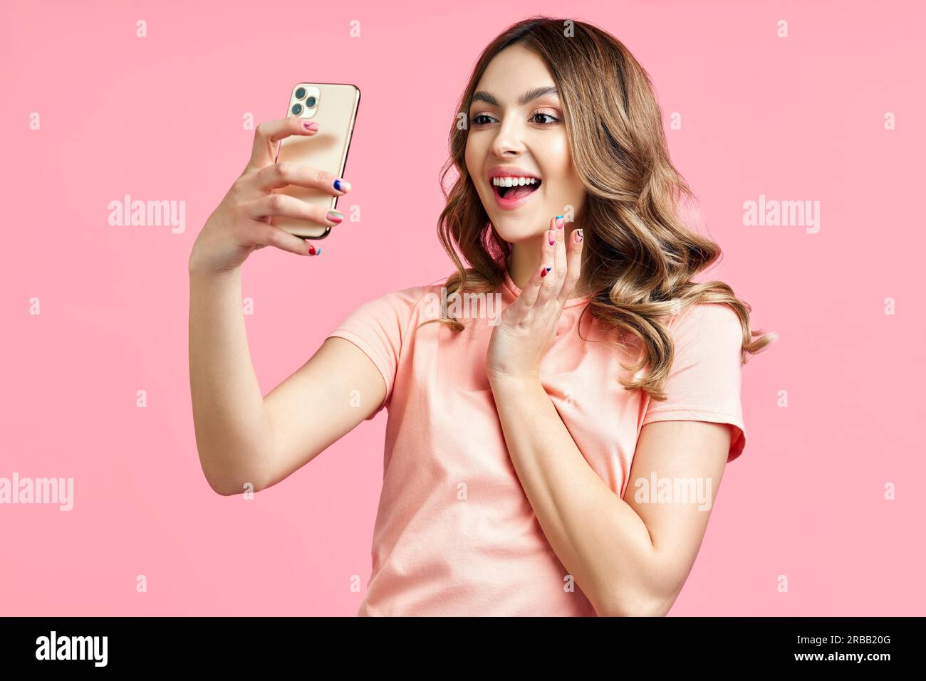 Giovane donna sorridente che effettua videochiamate utilizzando il telefono cellulare per comunicare con un amico su sfondo rosa, blogger o influencer femminile che parla per Foto Stock