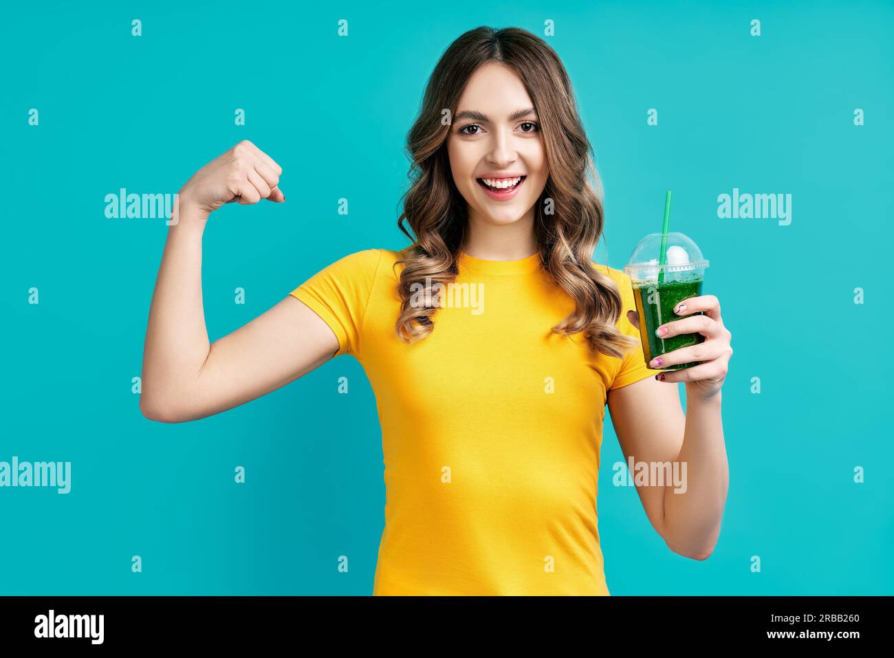 Bella giovane donna che tiene verde disintossicante succo di frullato vegetale e mostra i muscoli. Concetto di cibo sano Foto Stock