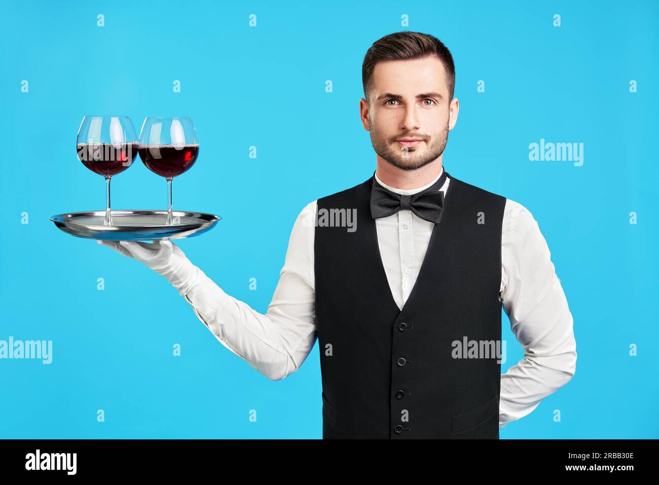 Elegante cameriere maschile con bicchieri di vino su sfondo blu. Celebrazione, concetto di ristorante Foto Stock