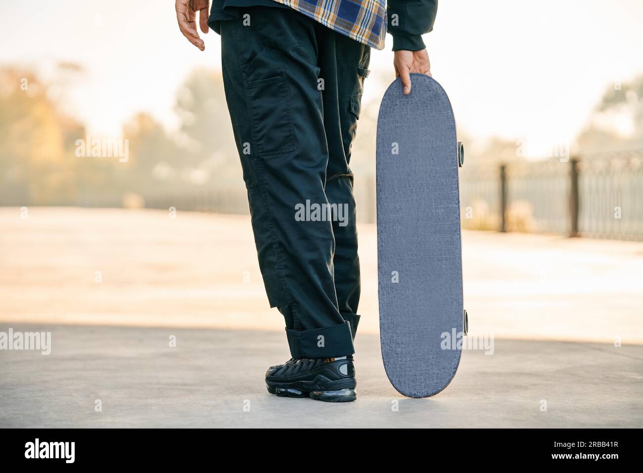 Immagine ritagliata dello skater che tiene lo skateboard sulla strada. Concetto di sport estremi Foto Stock