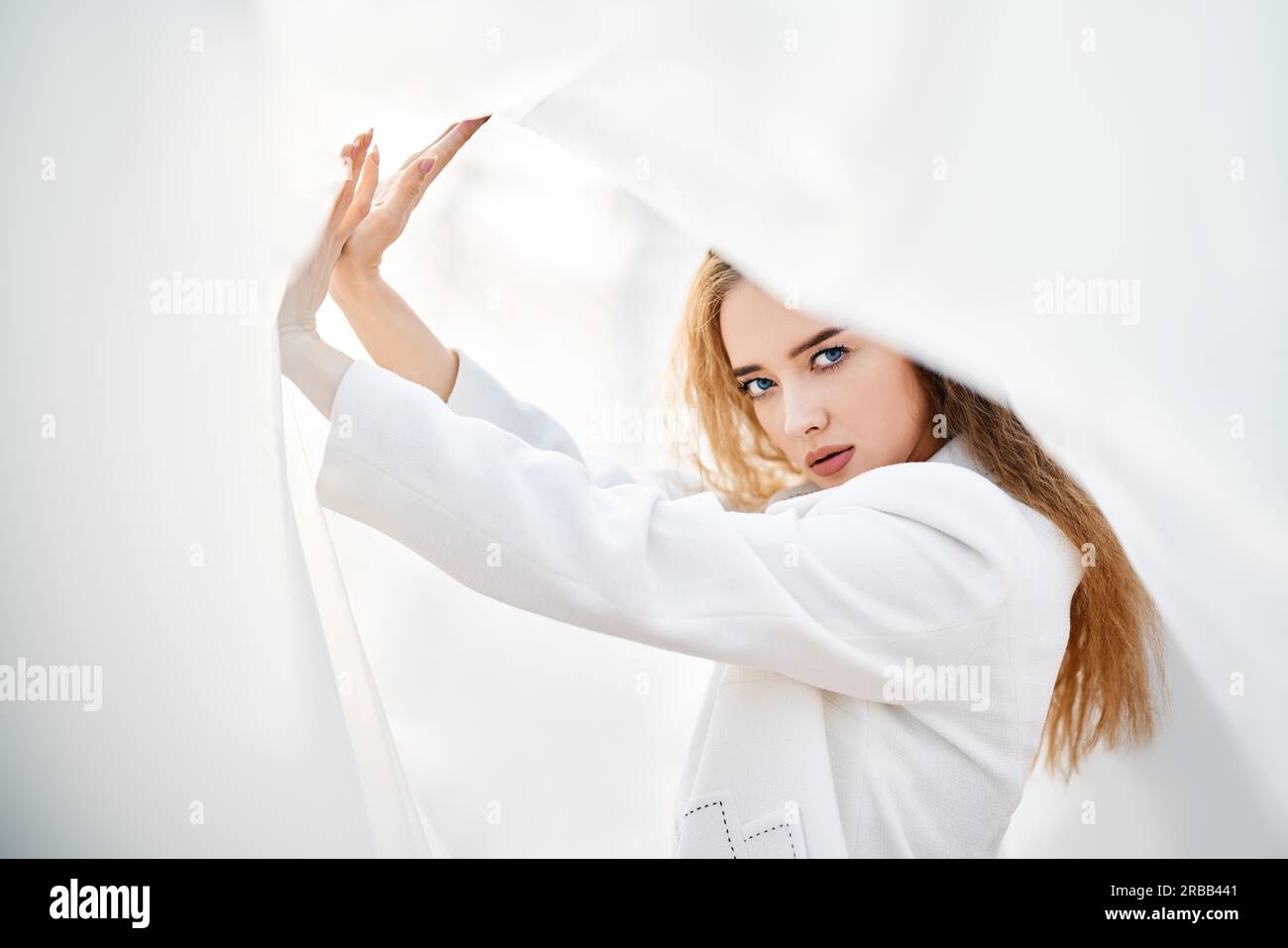 Giovane donna attraente in abiti bianchi in posa su sfondo astratto pallido guardando la macchina fotografica sicuro. Colori tenui e soleggiati. Concetto di bellezza Foto Stock