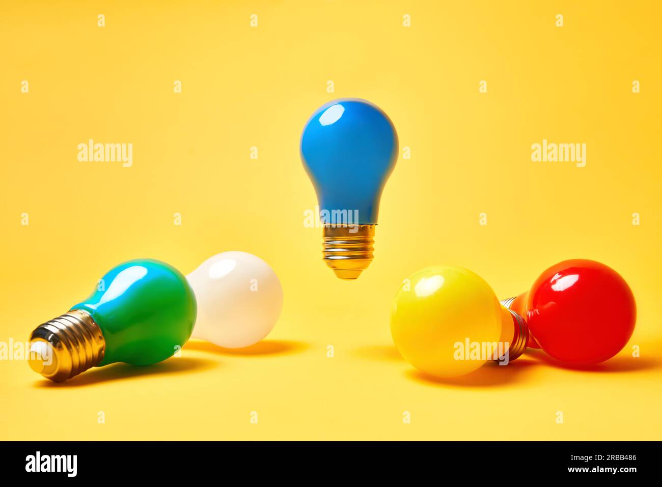 Layout creativo con lampadine multicolore su sfondo giallo. La lampadina blu levita in aria. Simbolo dell'idea, creatività aziendale, ispirazione Foto Stock