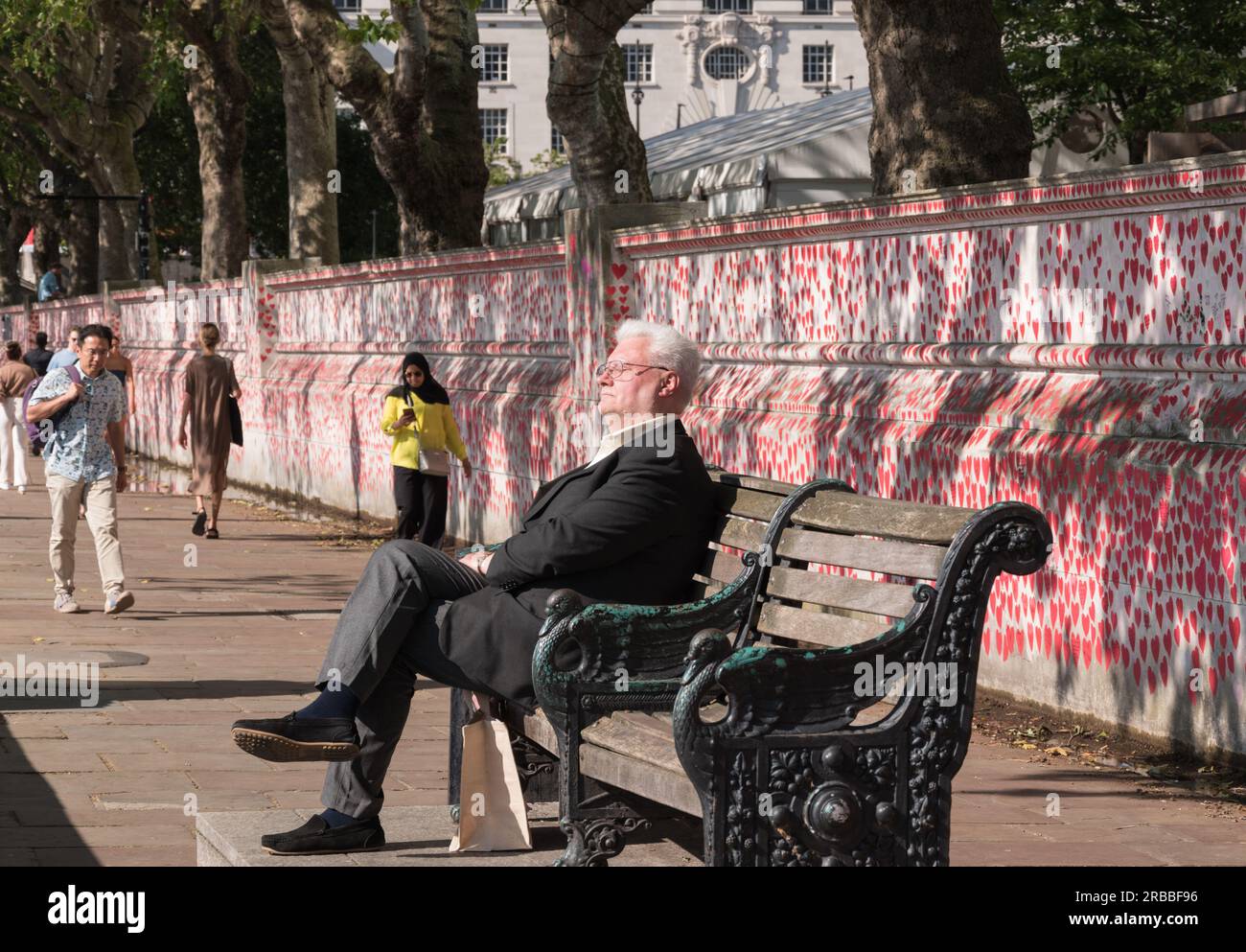 Un anziano seduto su una panchina del parco vicino al National Covid Memorial Wall, Londra, Inghilterra, Regno Unito. Foto Stock