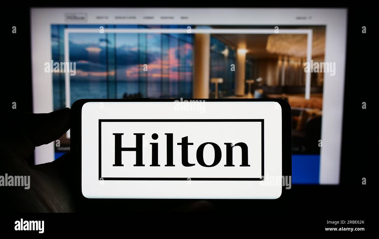 Persona che possiede un telefono cellulare con il logo della società americana Hilton Worldwide Holdings Inc. Sullo schermo davanti alla pagina Web. Concentrarsi sul display del telefono. Foto Stock