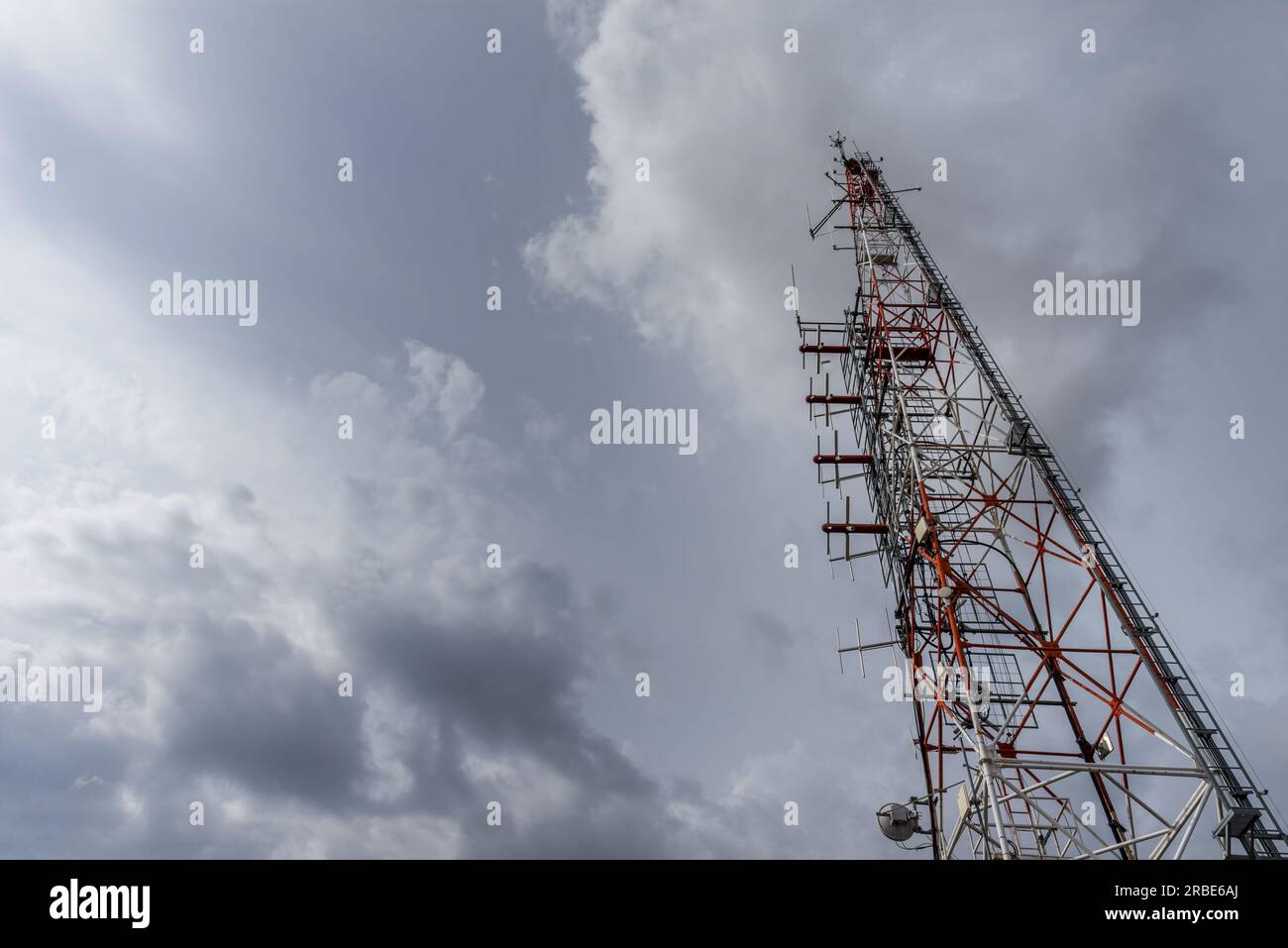 Un palo del ripetitore di telecomunicazioni e un cielo grigio e blu con nuvole dietro Foto Stock