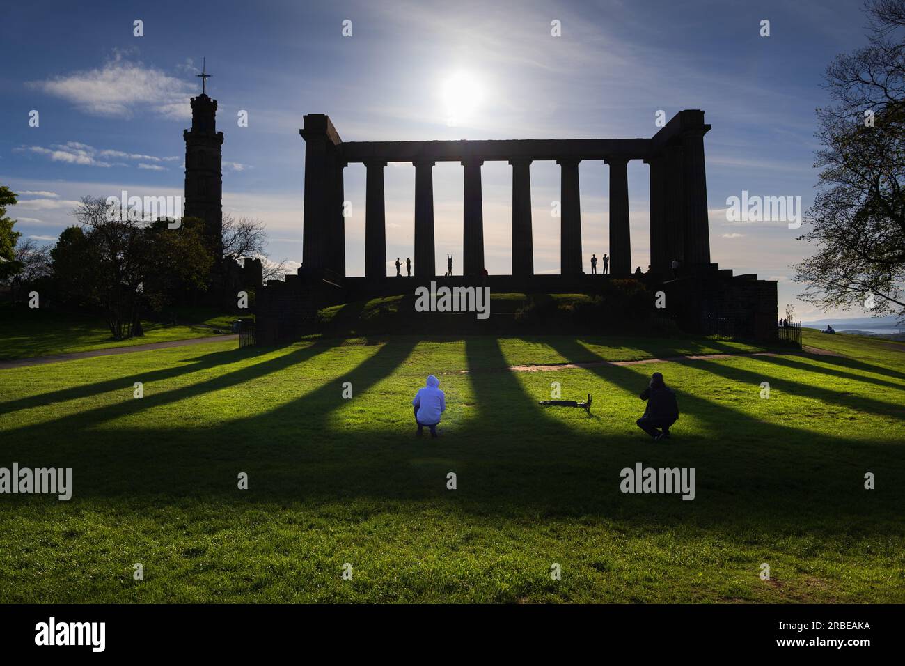 Calton Hill, Edimburgo, Monumento Nazionale di Scozia e Monumento Nelson contro la sagoma del sole con riflessi di ombre e luce solare, in ritardo dopo l'arrivo Foto Stock