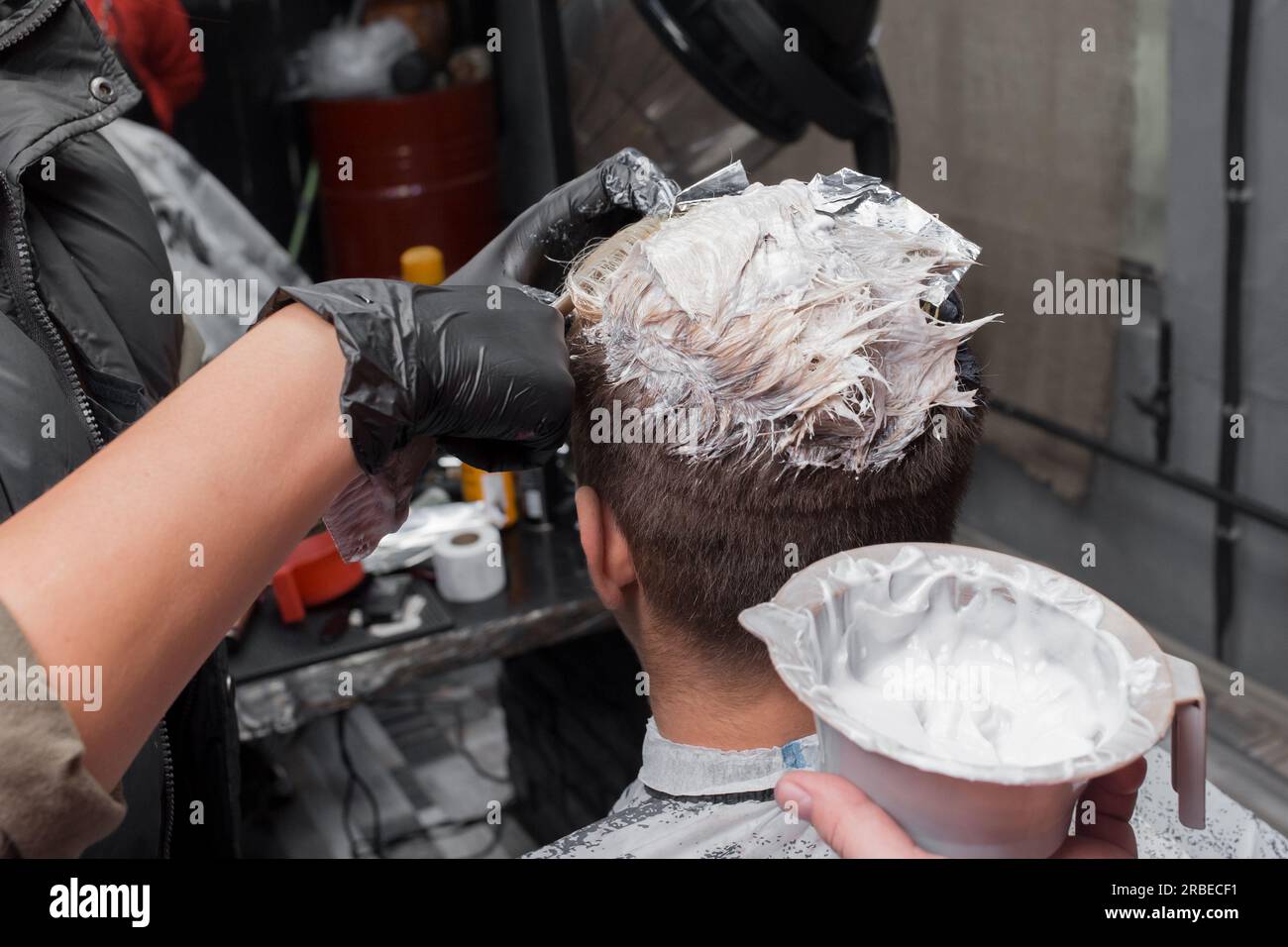 Mani di un barbiere professionista in guanti nel processo di colorazione dei capelli con tintura al lavoro in un parrucchiere. Foto Stock