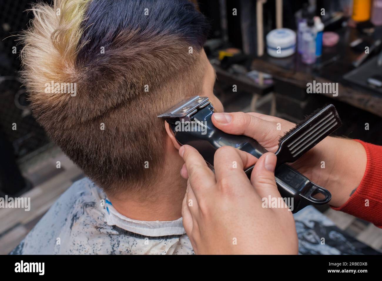 Le mani di un uomo, di un artigiano professionista, di un lavoratore di salone, tagliano i capelli con una macchina a un cliente nell'area dell'orecchio. Foto Stock