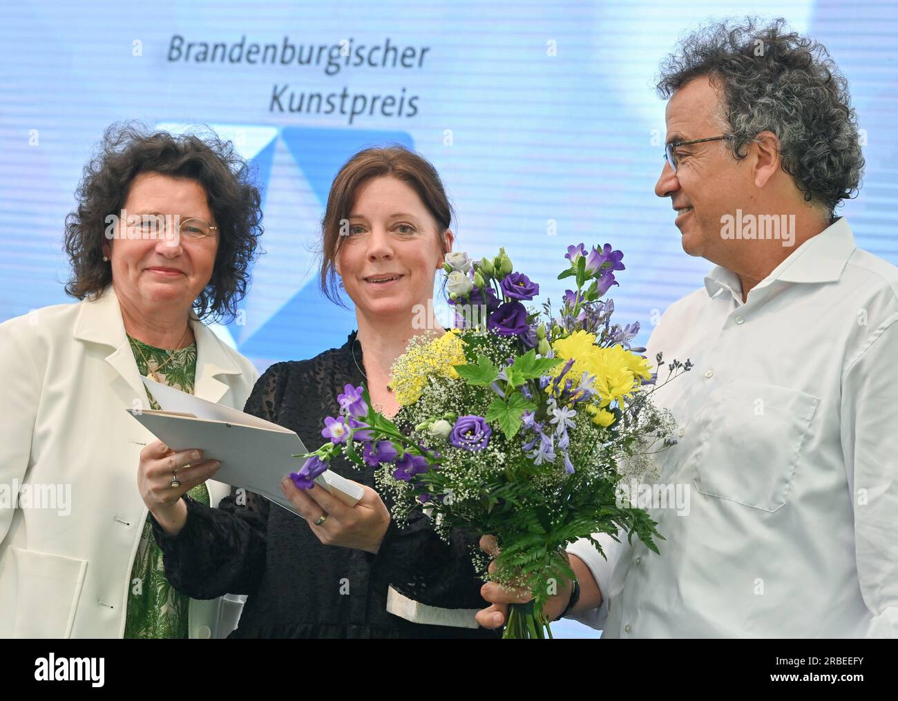 09 luglio 2023, Brandeburgo, Neuhardenberg: Kirstin Rabe (M), artista, riceve quest'anno il Brandenburg Art Award nella categoria grafica e installazione da Heike Kramer, Rappresentante generale dello Stiftung Schloss Neuhardenberg e da Frank Mangelsdorf, membro della giuria Art Award. Lo stesso giorno, il 20° Premio d'arte del Brandeburgo è stato assegnato dalla Fondazione Schloss Neuhardenberg e dal giornale Märkische Oderzeitung. Inoltre, ci sono due premi speciali. Nel 2023, il premio sarà sostenuto per la prima volta dalla Cancelleria di Stato del Brandeburgo in qualità di partner. Gli espositori che li accompagnano Foto Stock