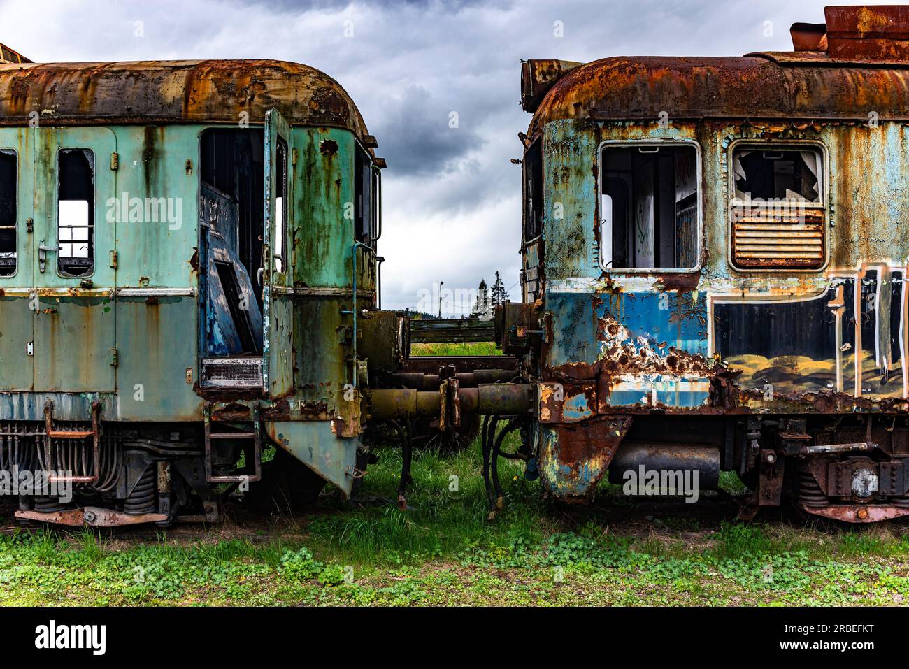 Il vecchio treno elettrico a più unità arrugginite è stato dismesso e abbandonato sulla banchina della ferrovia in un campo erboso verde Foto Stock