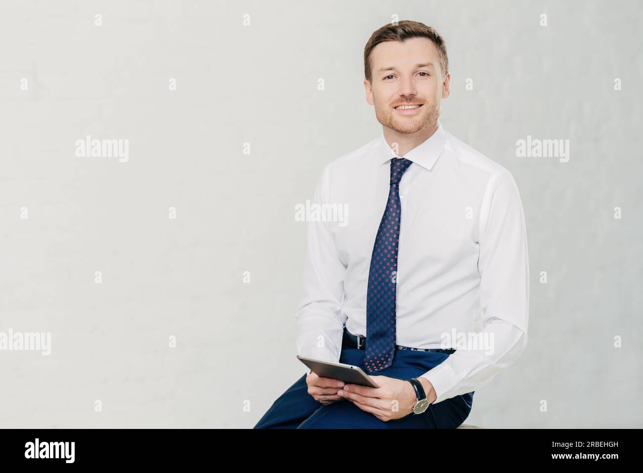 L'avvocato intelligente tiene un tablet, sorride, passa del tempo libero in ufficio. Isolato su sfondo bianco. Spazio per la copia disponibile per la pubblicità. Foto Stock