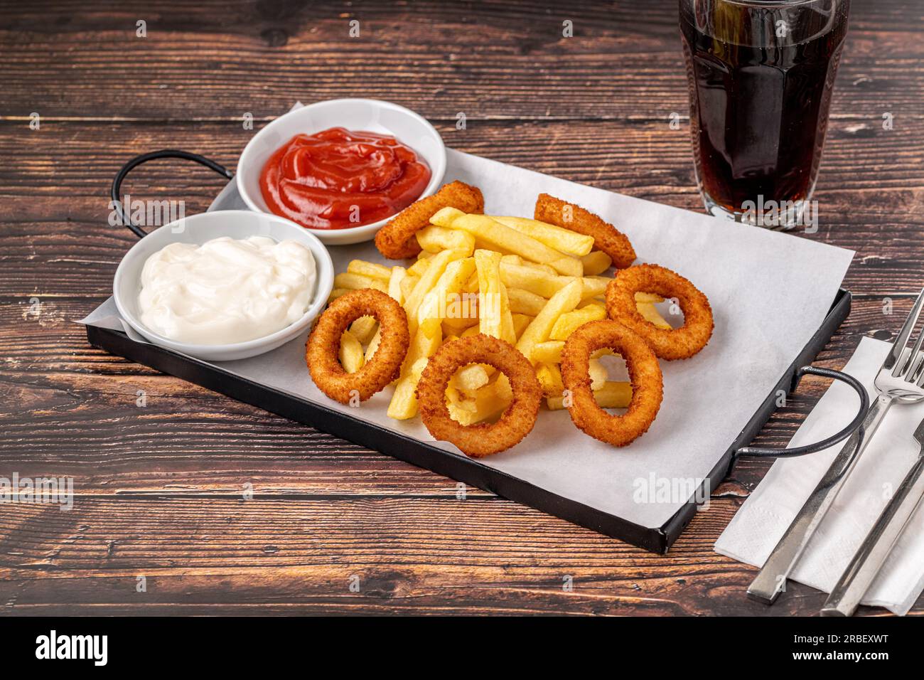 Anelli di cipolla e patatine fritte con ketchup e maionese su tavolo di legno Foto Stock