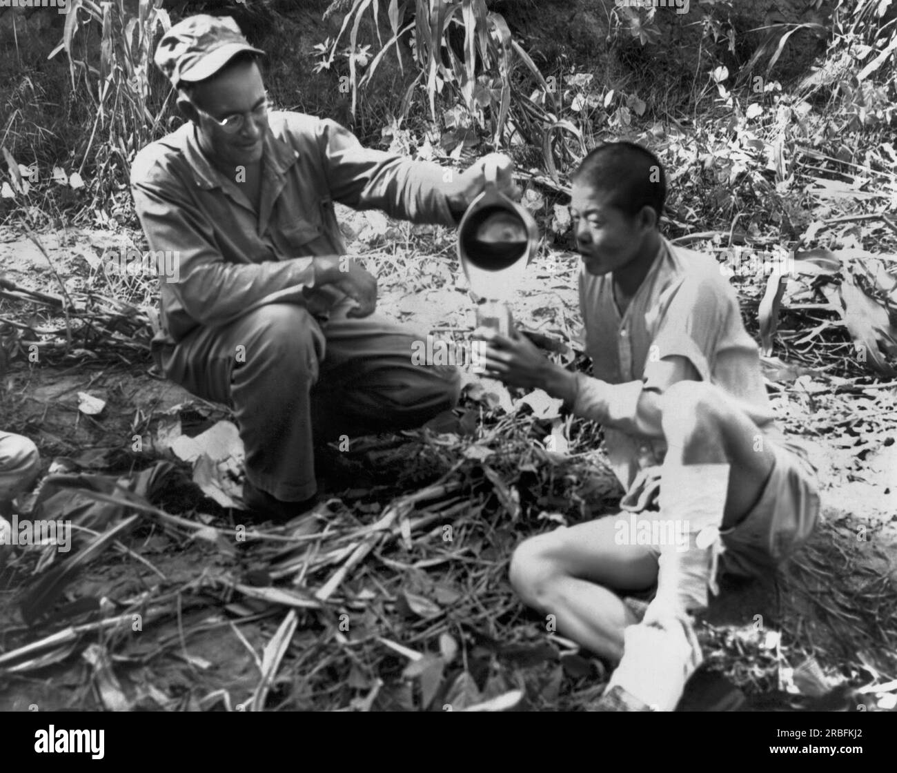 Corea: 5 ottobre 1950 Un medico della Marina che serve con i Fifth Marines dà una bevanda d'acqua a un POW nordcoreano dopo aver ricevuto cure per un piede ferito. Foto Stock