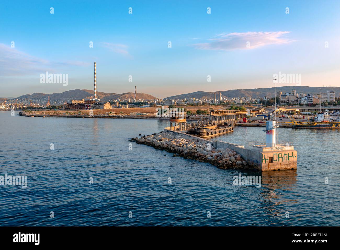 L'ingresso del porto del Pireo in Grecia, con il frangiflutti e la città del Pireo con i fumogeni di fabbrica sullo sfondo. Foto Stock