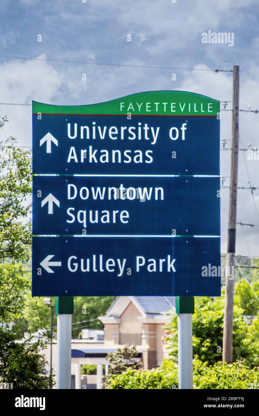 Segui le indicazioni per la University of Arkansas e per il centro di Square e Gulley Park, con lo sfondo sfocato di alberi ed edifici Foto Stock