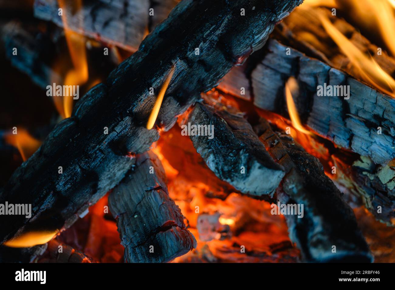 I tronchi di legno stanno bruciando nel caminetto. primo piano. Lingue di fiamma su sfondo scuro. Foto Stock