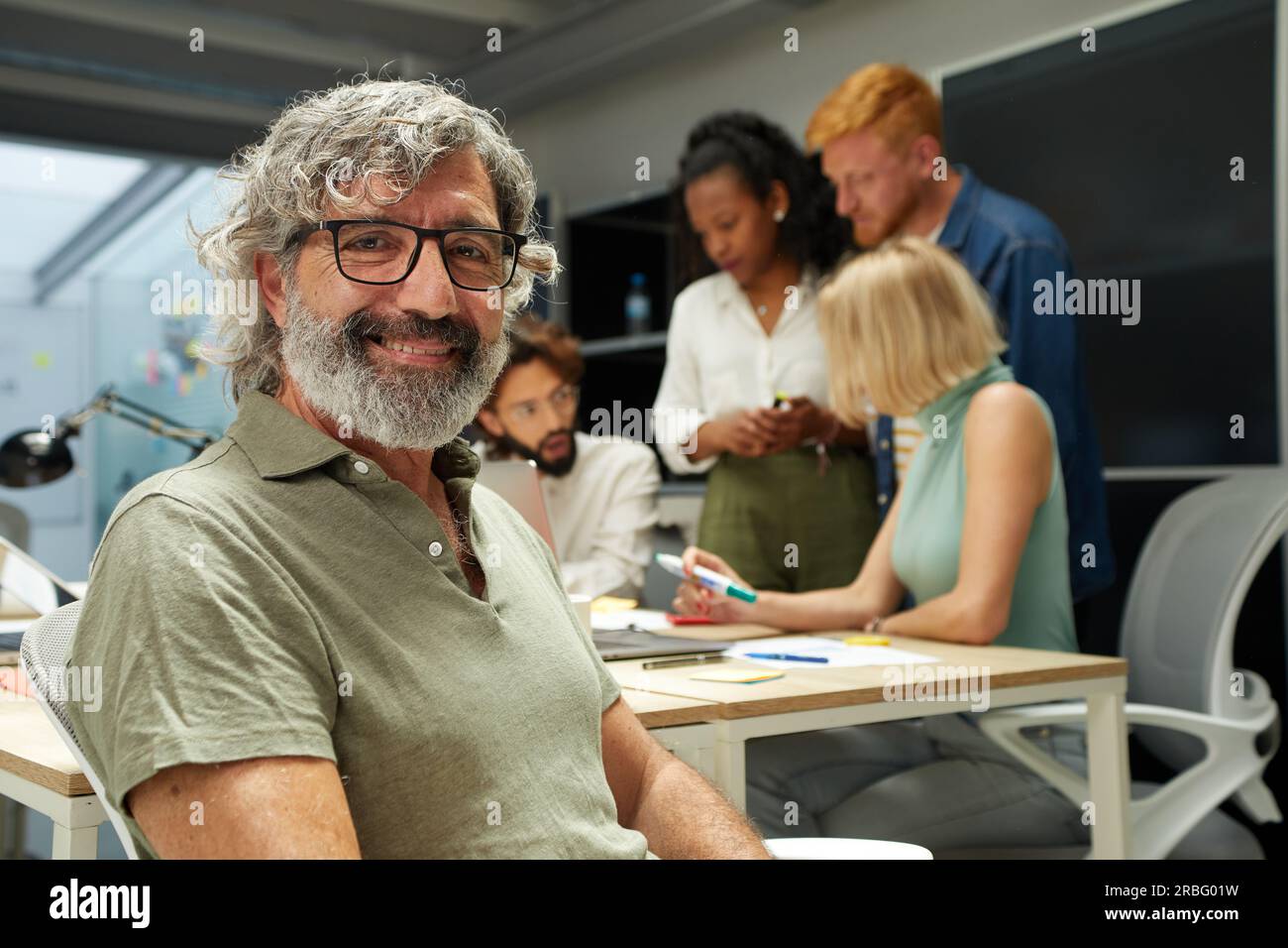 Ritratto dell'uomo d'ufficio che sorride e guarda la fotocamera. Sullo sfondo c'è un gruppo di persone Foto Stock