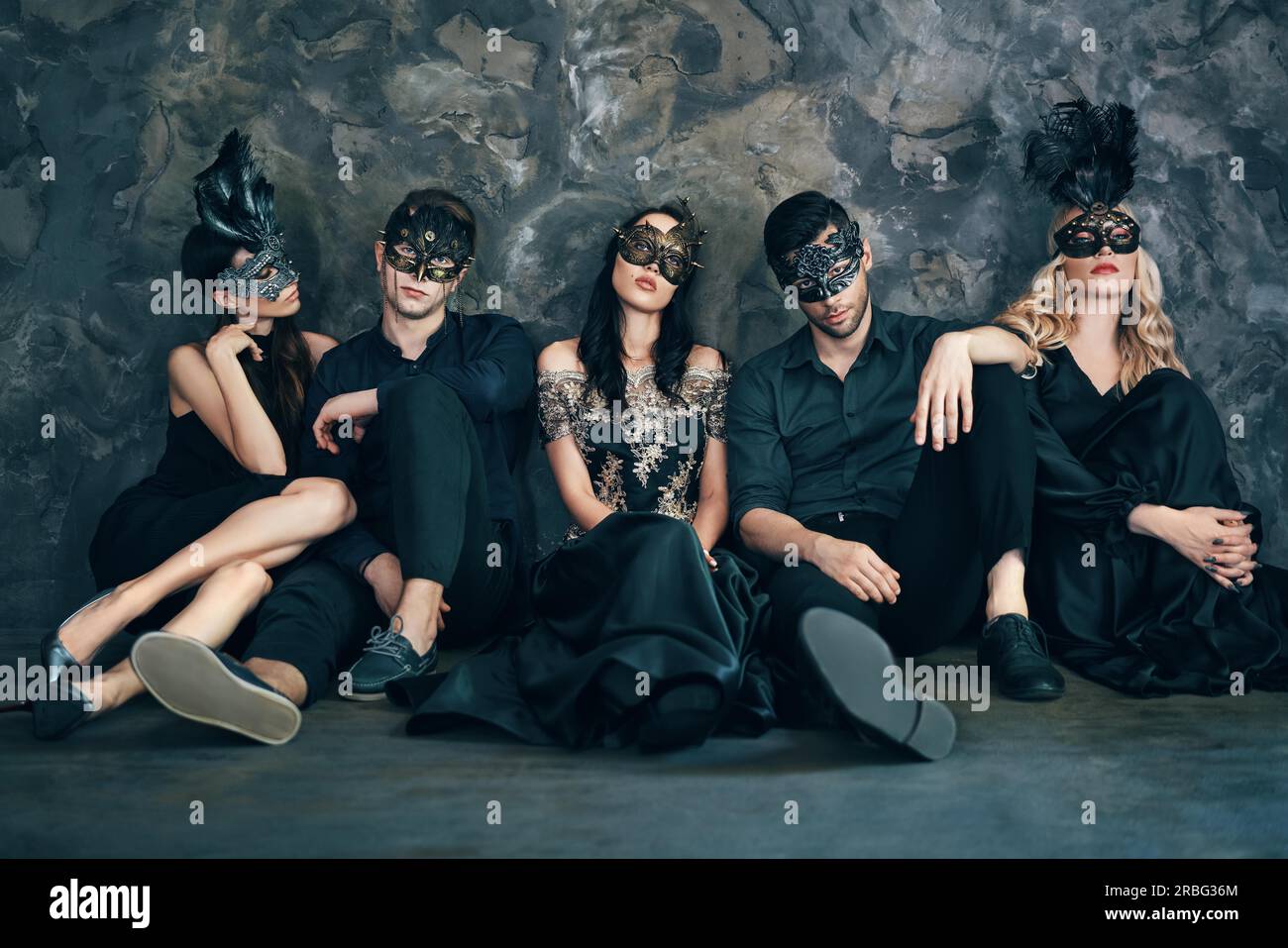 Gruppo di amici in maschera di carnevale seduti sul pavimento rilassarsi dopo la festa. Belle donne e uomini che indossano una maschera veneziana. Moda, amici Foto Stock