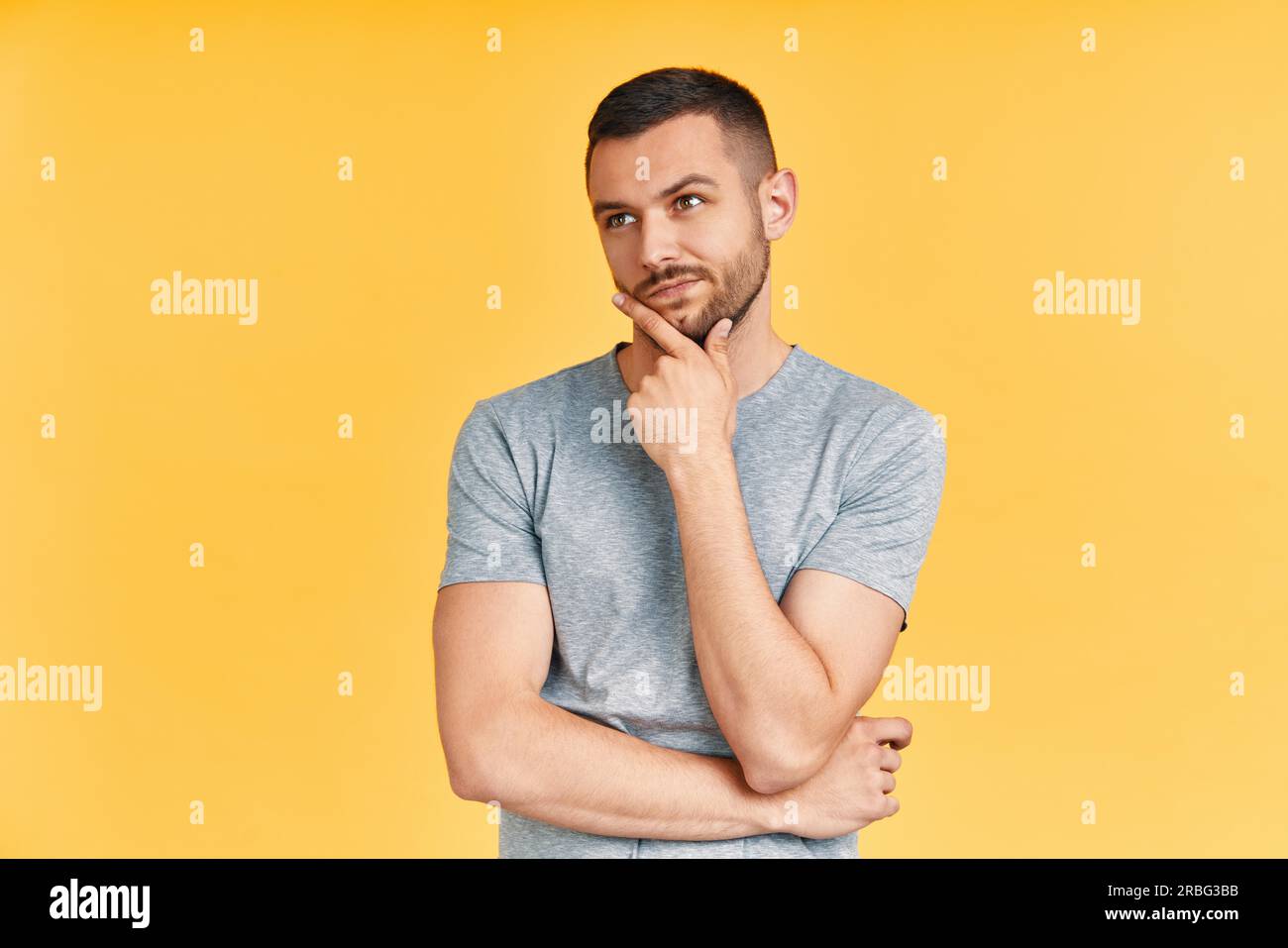 Giovane uomo premuroso pensiero e guardando a parte sulla copia spazio isolato su sfondo giallo. Voce maschile tenendo la mano sul mento. Dubbio, soluzione, decisione e Foto Stock