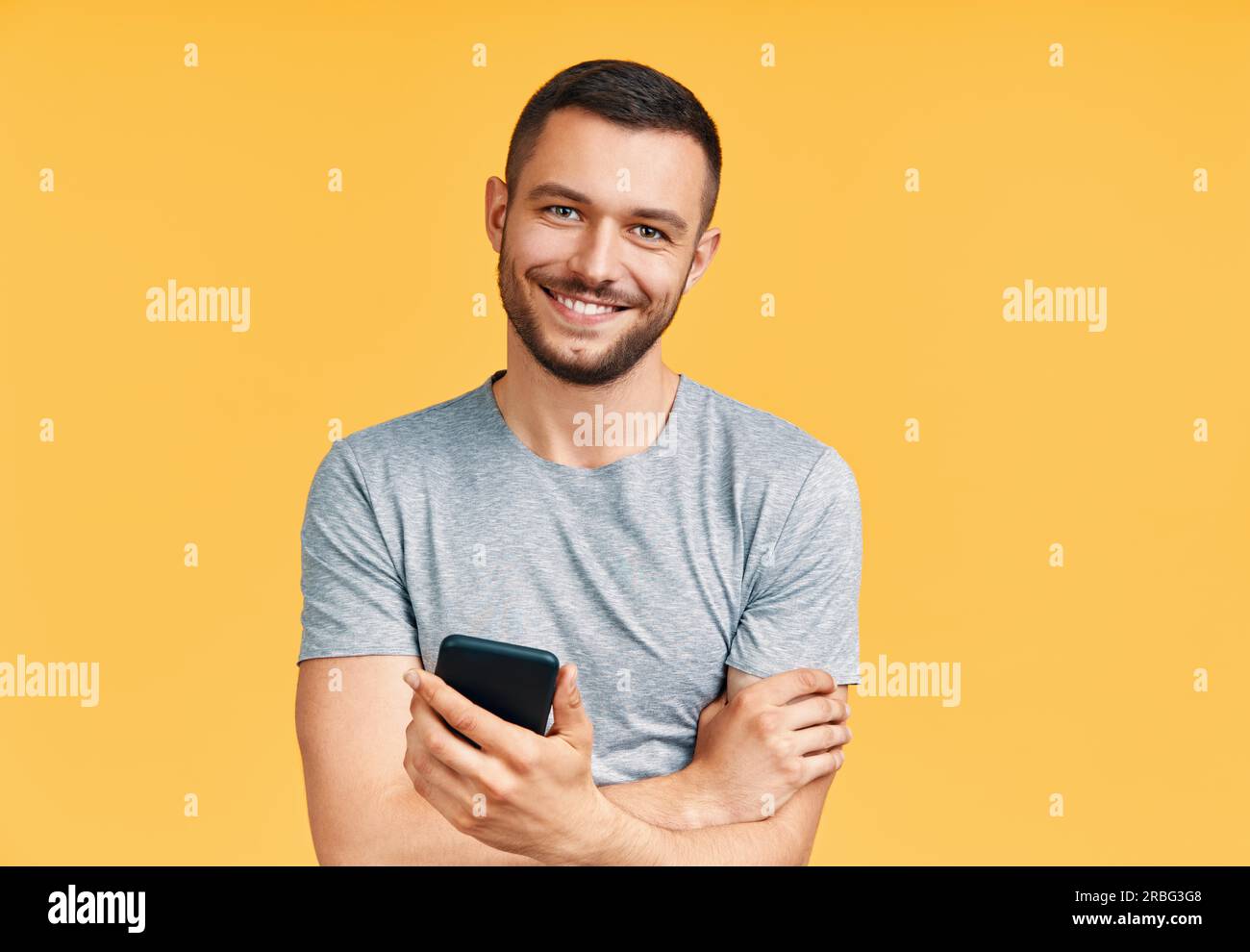 Bel uomo sorridente tenendo il telefono cellulare e cercando di telecamera in giallo di sfondo per studio. Concetto di comunicazione Foto Stock