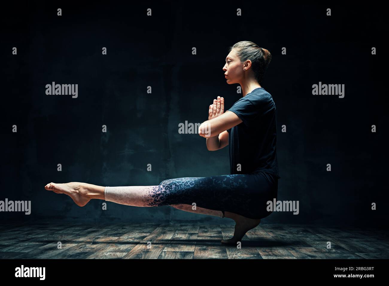 Giovane bella donna che fa yoga asana in punta di piedi posa prapadasana variazione in camera buia. Praticare yoga, benessere, concetto di benessere Foto Stock