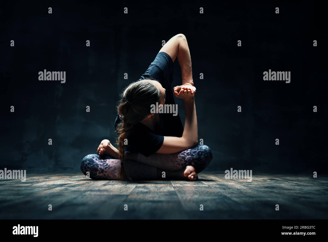 Giovane donna fare yoga Padmasana pongono variazione sulla camera oscura. La pratica dello yoga, benessere, il concetto di benessere Foto Stock