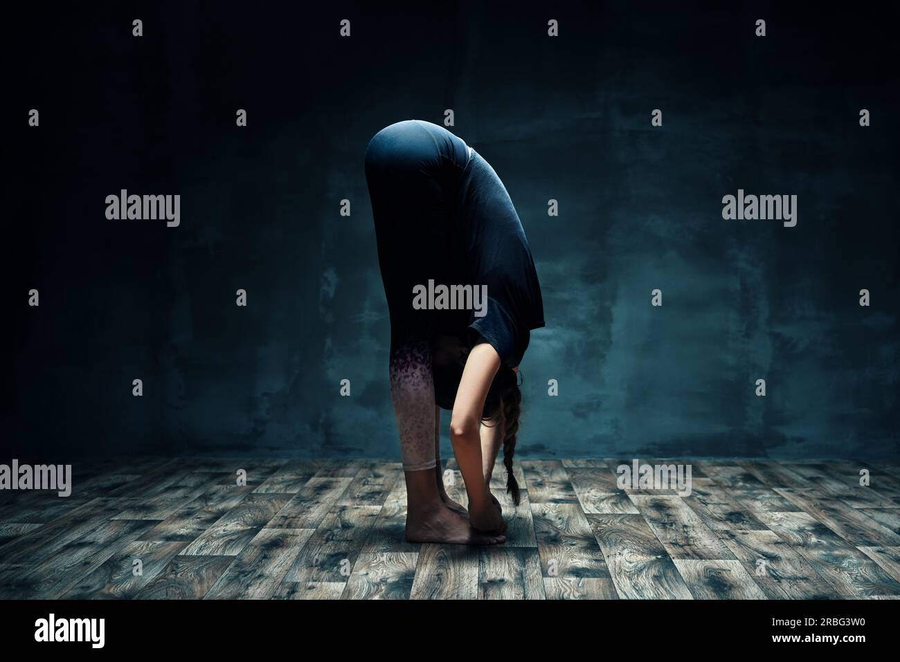 Giovane donna fare yoga permanente di piegare in avanti pone in camera oscura. Benessere, sport e stile di vita sano. Uttanasana Foto Stock