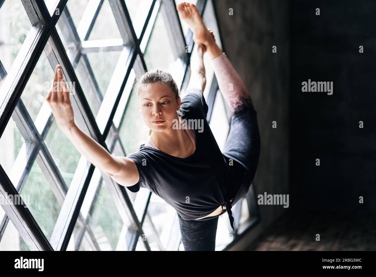 Giovane bella donna che fa yoga asana natarajasana su grande sfondo triangolare della finestra. Benessere, meditazione e stile di vita sano. Signore della danza Foto Stock