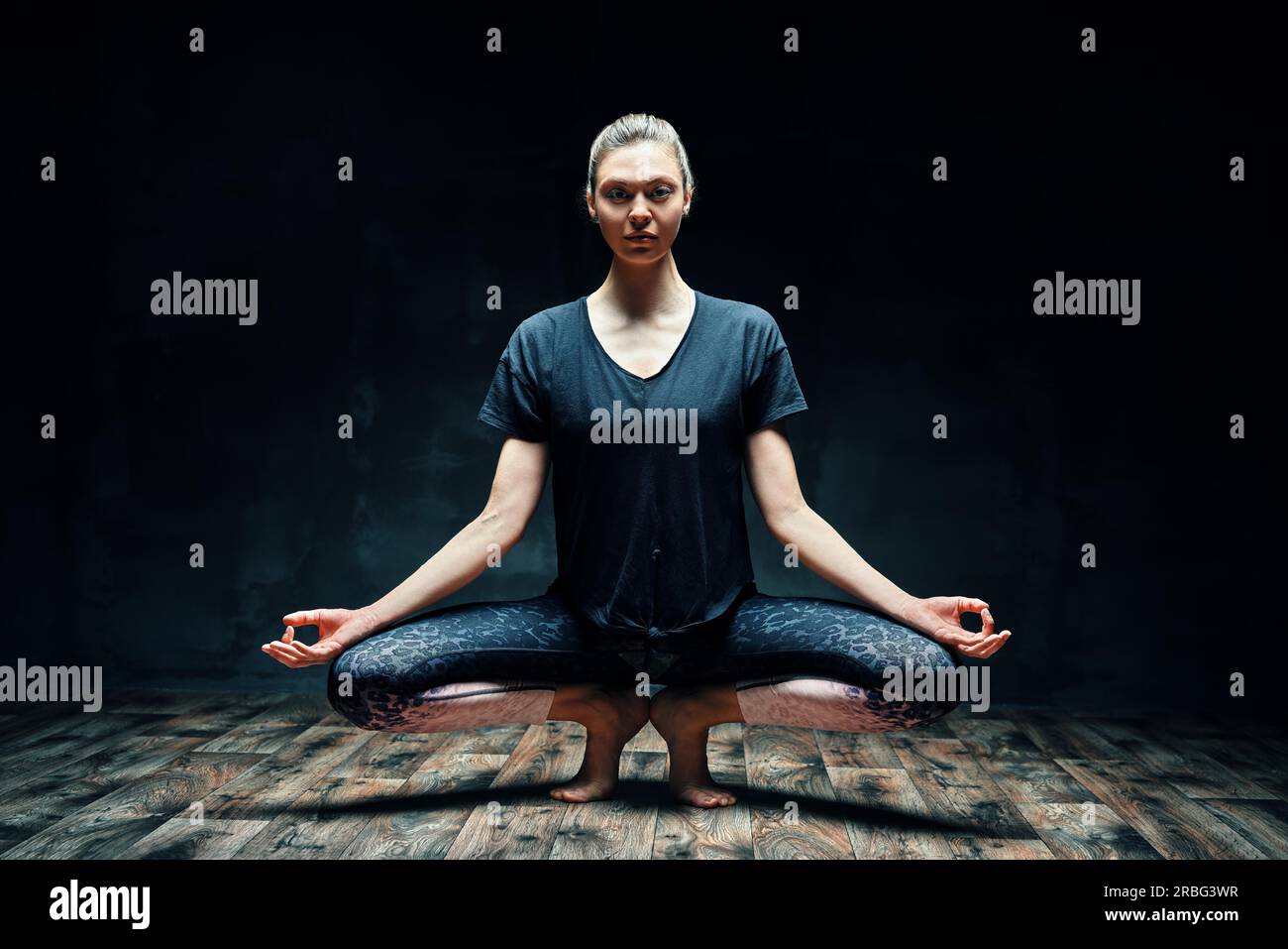 Giovane bella donna che fa yoga asana in punta di piedi posa prapadasana variazione in camera buia. Praticare yoga, benessere, concetto di benessere Foto Stock