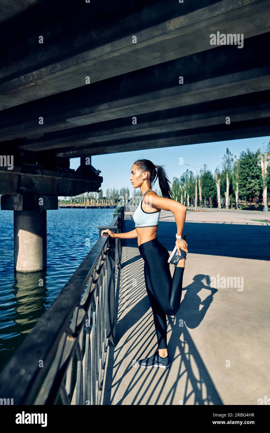 Donna sportiva che allunga le gambe per riscaldarsi prima di allenarsi. Concetto di allenamento urbano e corsa Foto Stock