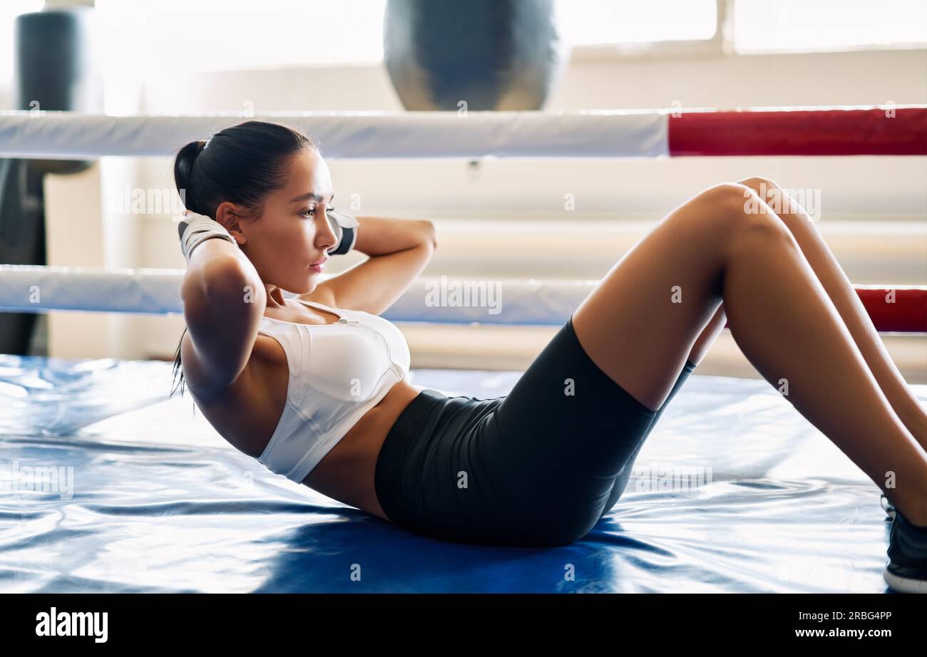 Donna in forma che fa esercizio fisico seduto sul tappeto nello studio di boxe. Allenamento di allenamento addominale per muscoli addominali Foto Stock