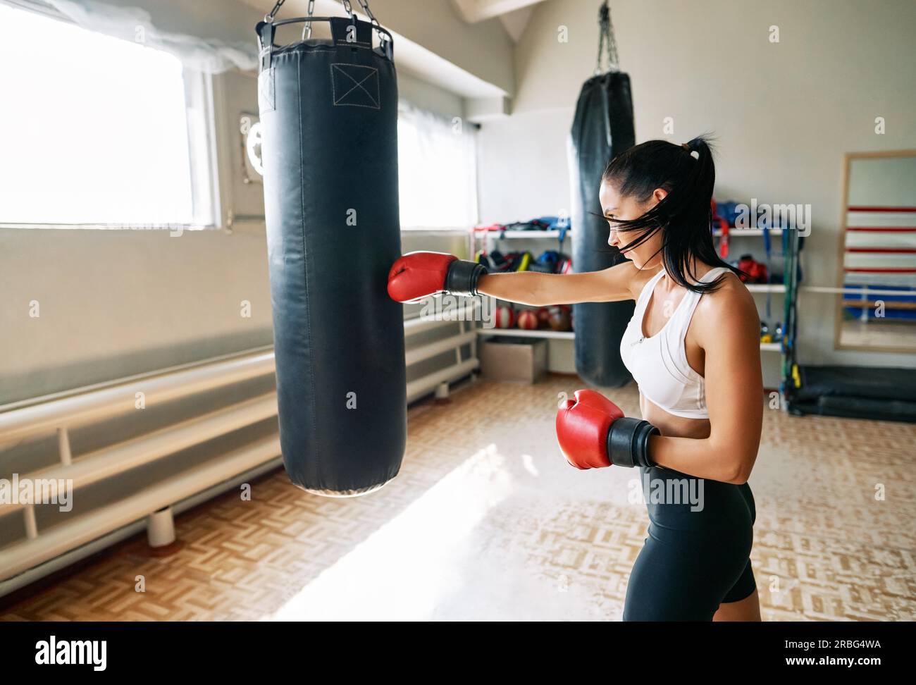 Pugile femminile che colpisce un enorme sacchetto di punzonatura in palestra fitness. Donna che pratica i suoi pugni in uno studio di boxe Foto Stock