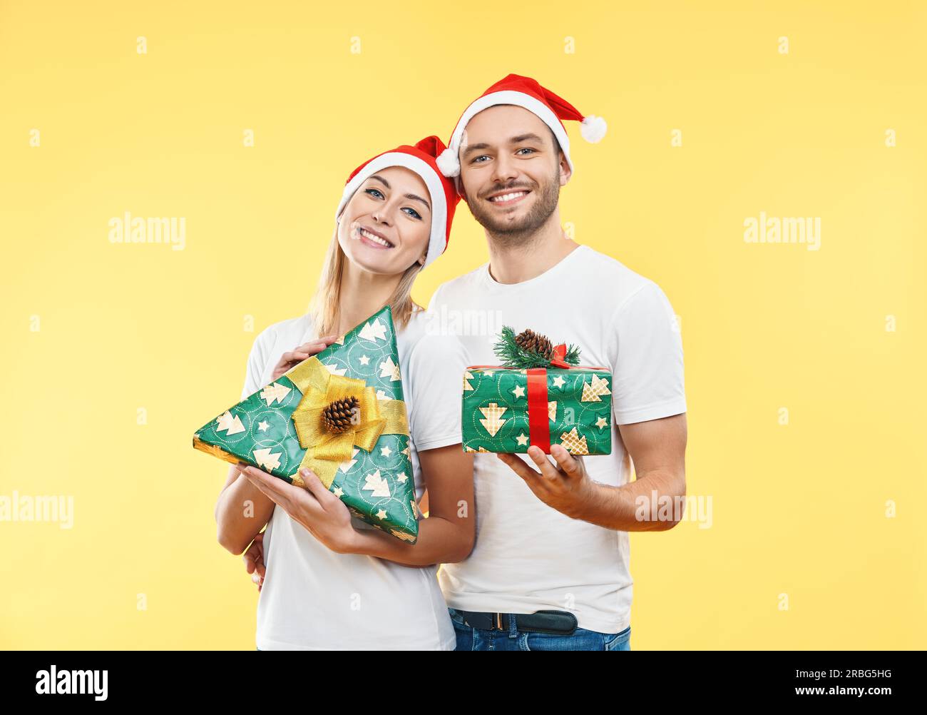 Giovane coppia felice con scatole regalo di Natale su sfondo giallo. Presente, vacanza, celebrazione concetto Foto Stock