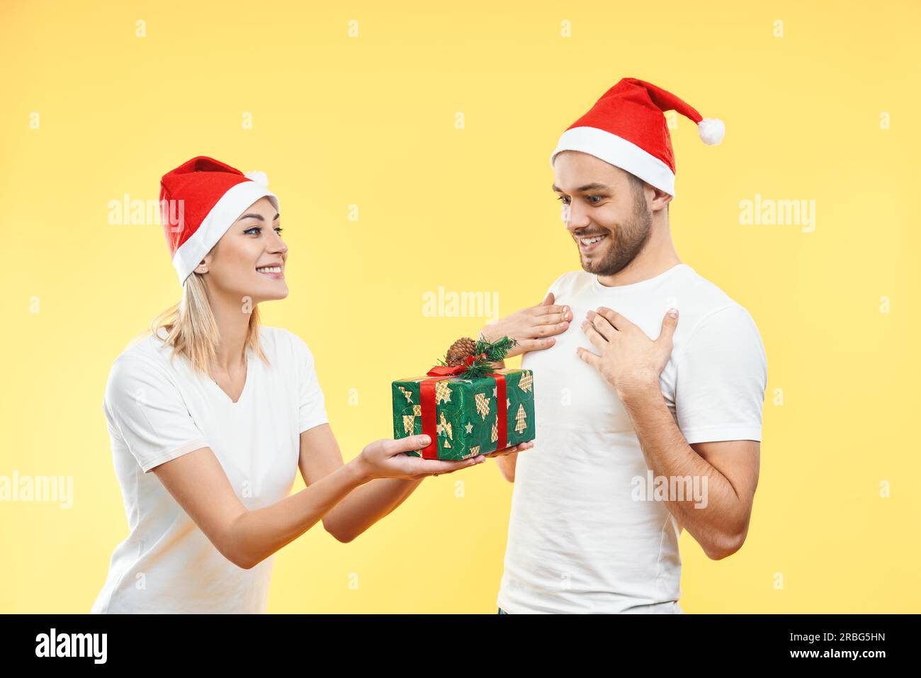 Giovane donna dare scatola regalo di natale a uomo isolato su sfondo giallo. Presente, vacanza, celebrazione concetto Foto Stock