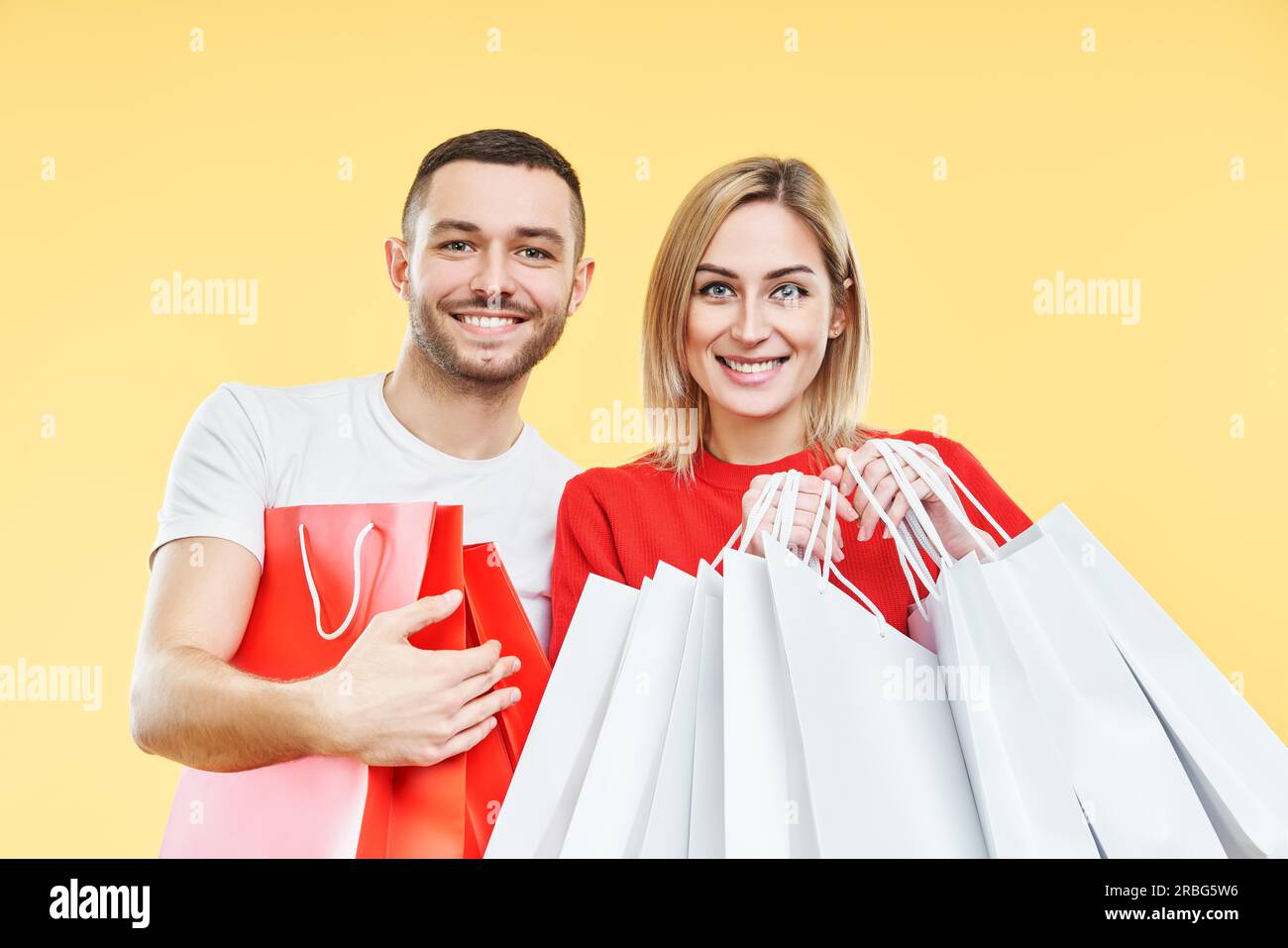 Giovane coppia felice che tiene i sacchetti di shopping nelle mani su sfondo giallo. Vendita, er, cliente, concetto di sconto Foto Stock