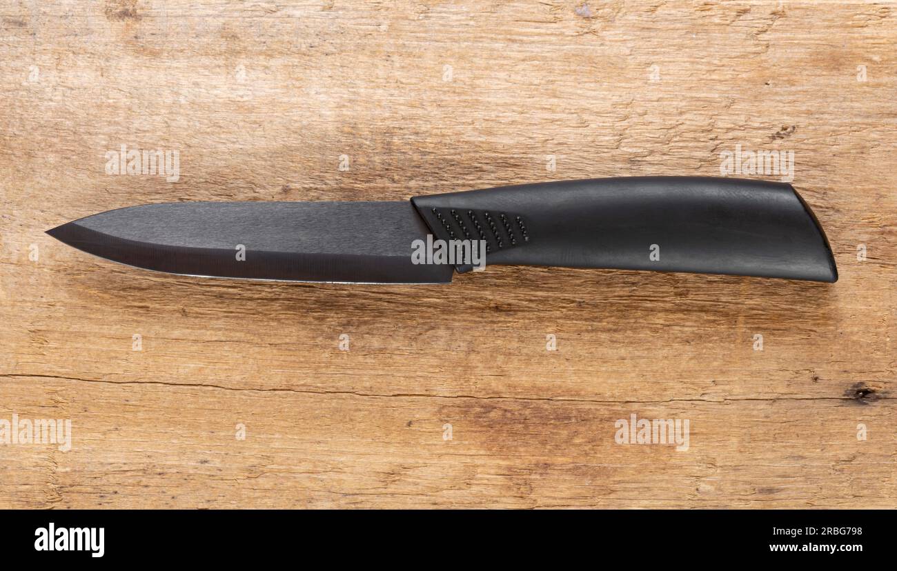 Coltello da cucina, con manico nero e lama in acciaio nero su sfondo in legno naturale Foto Stock