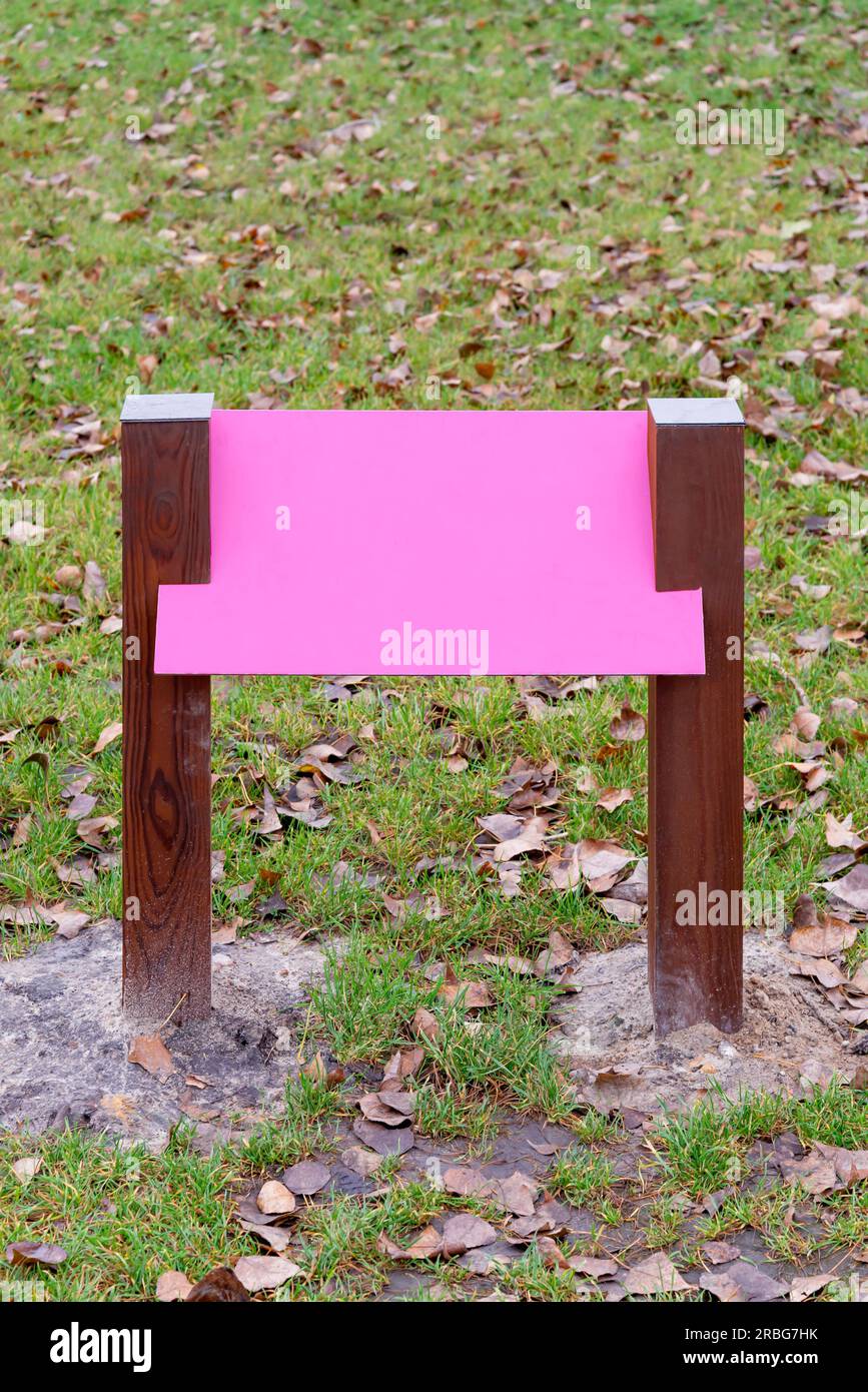 Rosa Bianco tavola di legno per informazioni e indicazioni nel parco, con uno sfondo di erba verde coperta da foglie di autunno Foto Stock