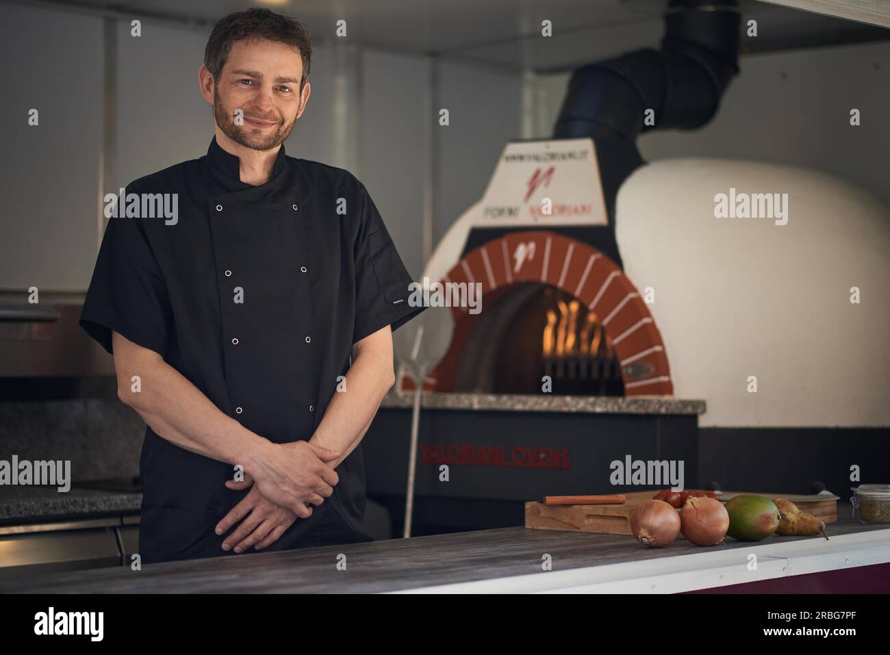 Lo chef sorridente la cottura o la cottura a fiamma una pizza italiana in un moderno forno a legna in una pizzeria Foto Stock