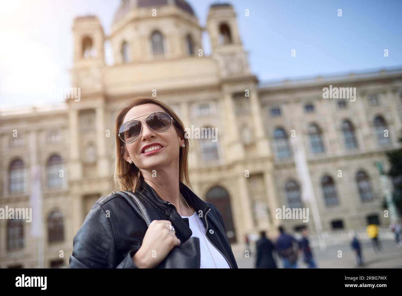 Attraente donna sorridente in occhiali da sole alla ricerca permanente da parte di fronte a un grande edificio storico in un basso angolo di visione Foto Stock