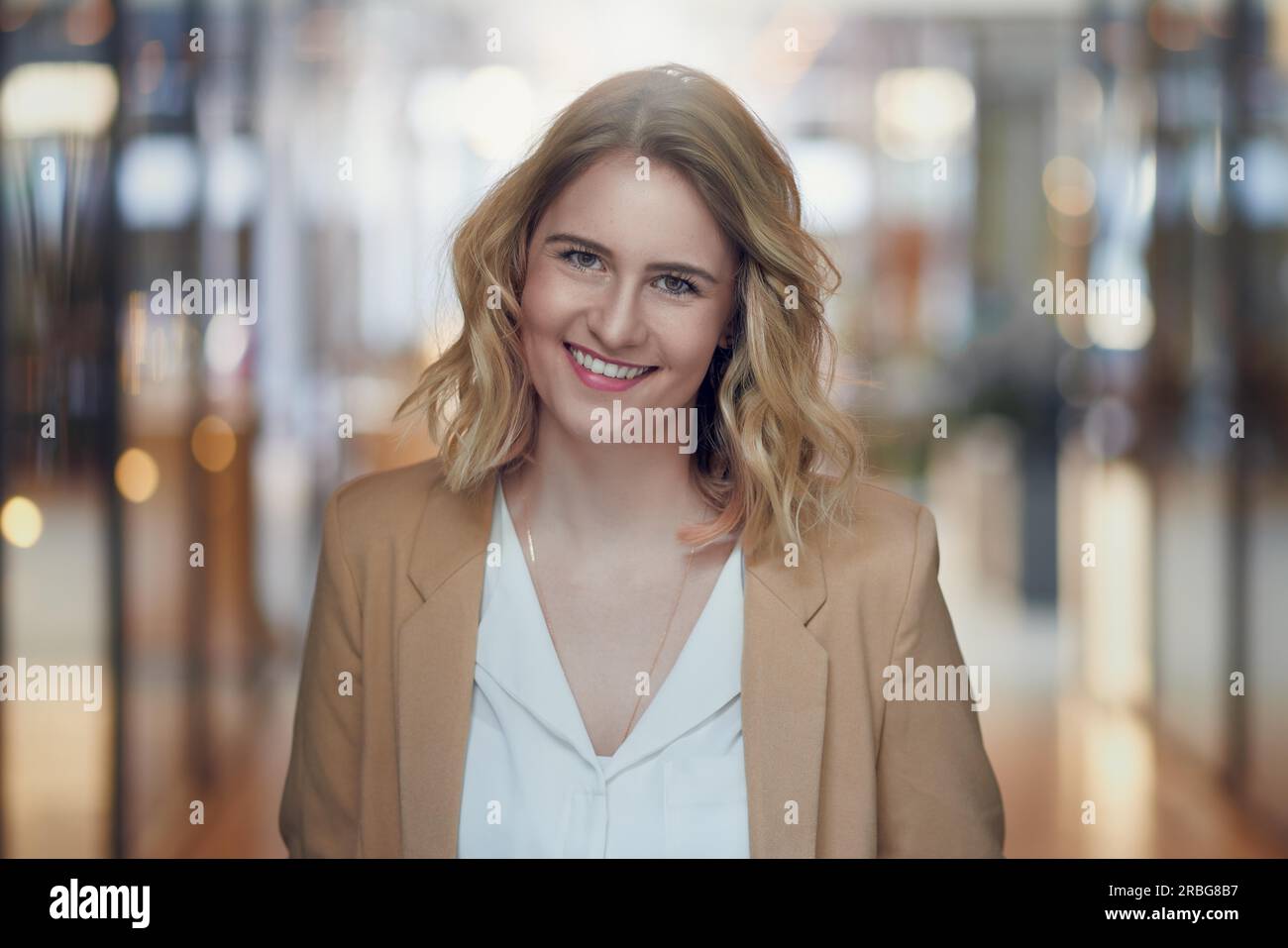 Attraente giovane donna bionda con un dolce sorriso in posa di un arcade in una testa e spalle ritratto guardando la fotocamera Foto Stock