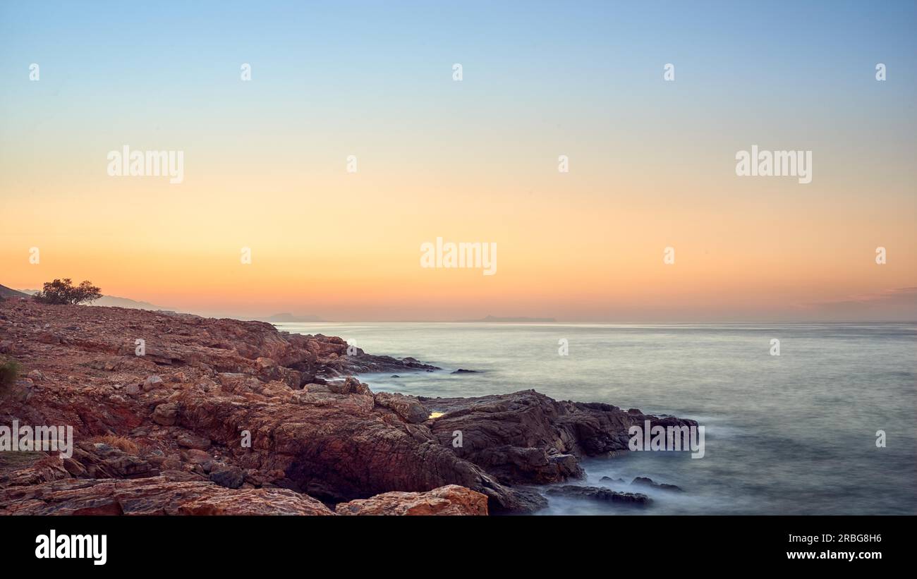 Colorato arancione tramonto tropicale al di sopra di una costa rocciosa con un oceano di calma e ad incandescenza oltre l'orizzonte Foto Stock