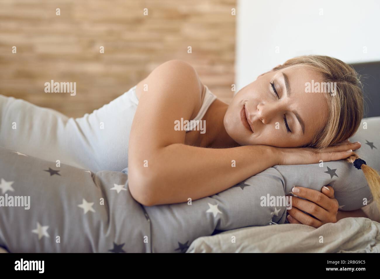 Bella giovane donna incinta che dorme con uno speciale cuscino di supporto che corre per tutta la lunghezza del suo corpo in una vista ravvicinata e serena Foto Stock