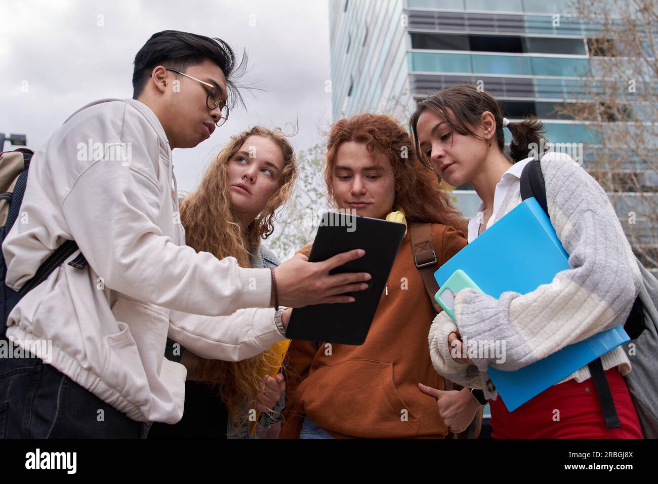 Gruppo di studenti che condividono un tablet digitale per controllare Internet in piedi fuori dal campus Foto Stock