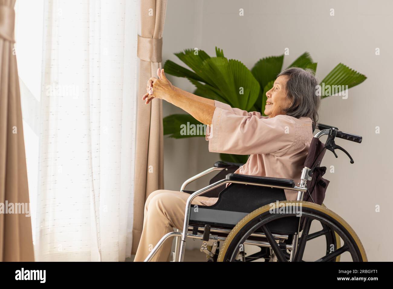 donna asiatica anziana che fa esercizi di stretching su sedia a rotelle nel soggiorno di casa Foto Stock