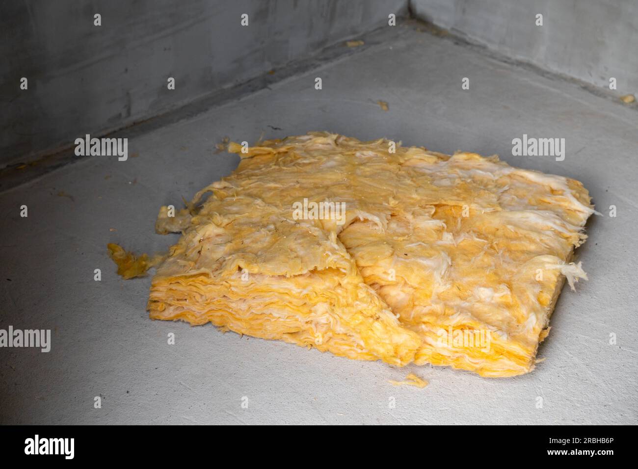 Il resto della lana di vetro giallo giace sul pavimento di cemento, da vicino. Materiale isolante e insonorizzante universale Foto Stock